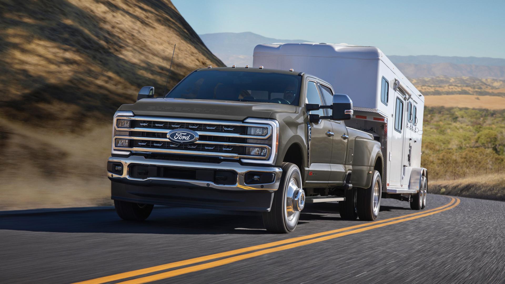 2027 Ford Super Duty® F-350® Lariat® model with the Chrome Package driving on a hilly paved road while towing a large trailer