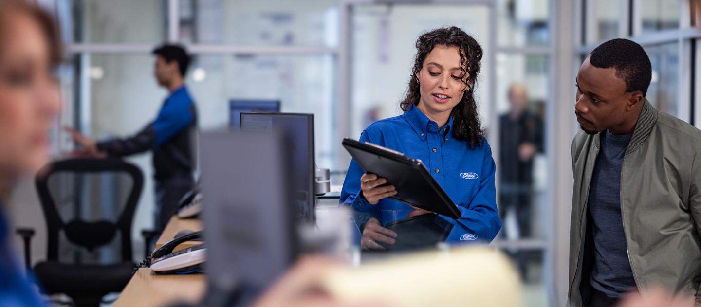 Ford employee holding a tablet speaking with a customer.
