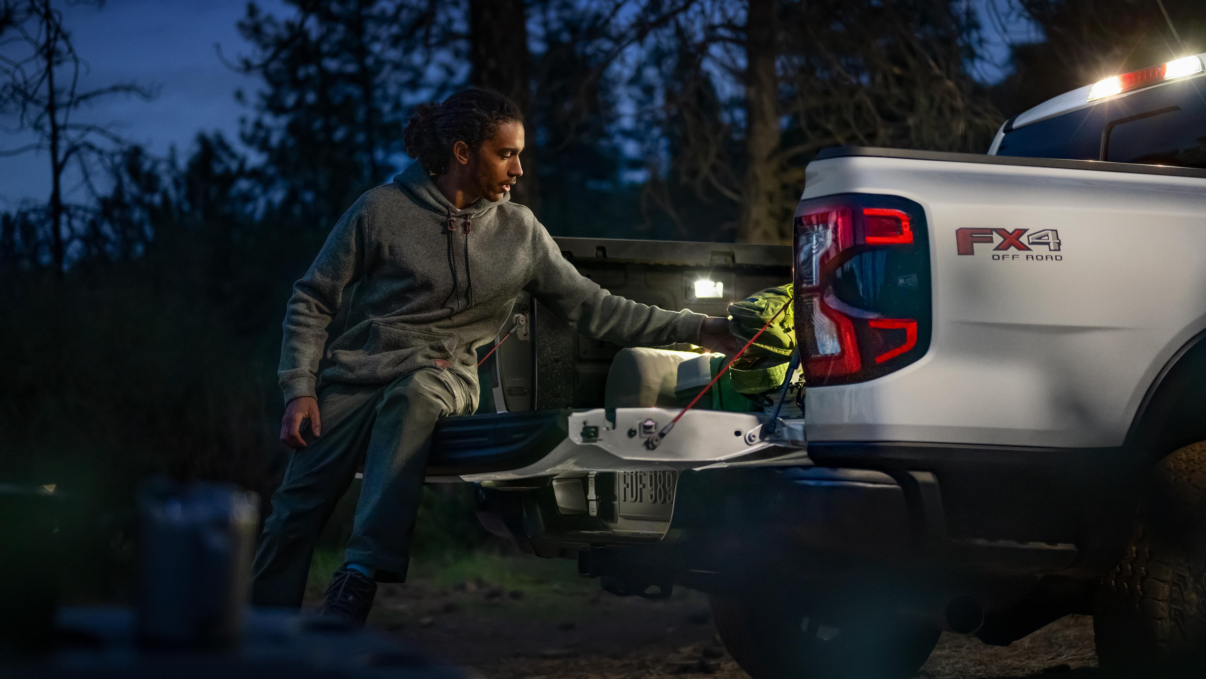 A person loading gear into the bed of their 2026 Ford Ranger® truck while sitting on the open tailgate