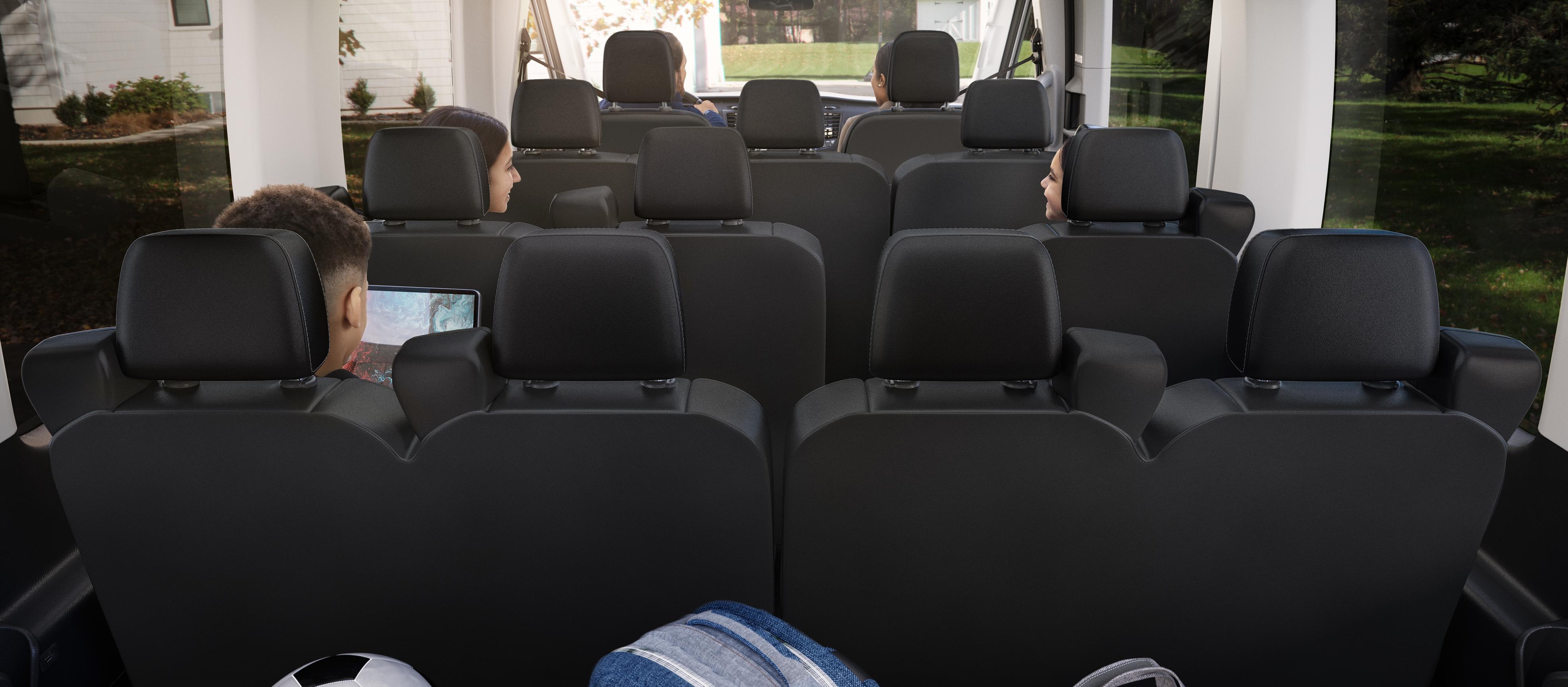 Interior of a 2027 Ford Transit® passenger van with multiple rows of black seats occupied by children, viewed from the back