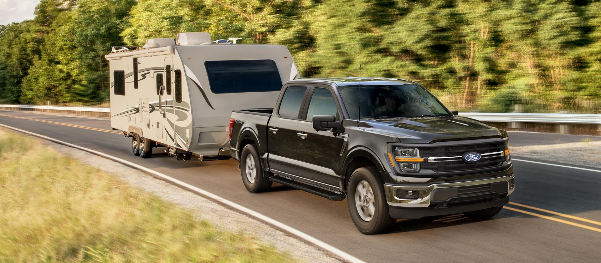 2025 Ford F-150® XLT pickup pulling a camper on a tree-lined road