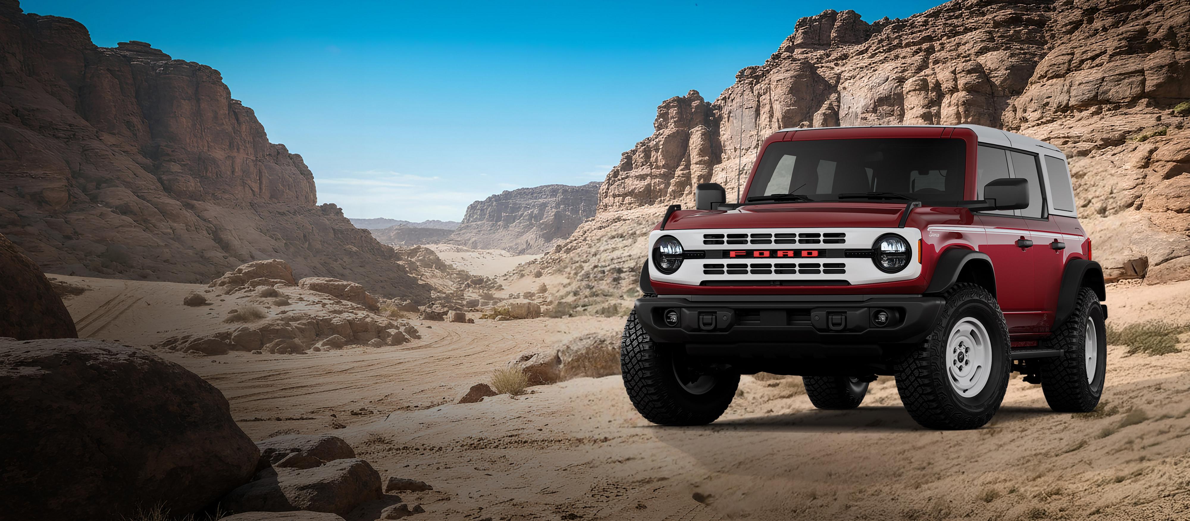 A 2026 Ford Bronco® Heritage Edition model shown in Ruby Red Metallic Tinted Clearcoat parked on a rocky expanse
