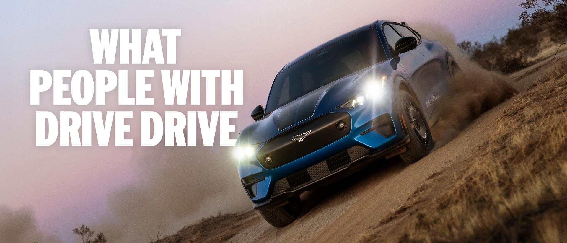 Three-quarter front view of a blue Ford Mustang Mach-E electric SUV driving on a dirt road at an angle. "What people with drive drive."