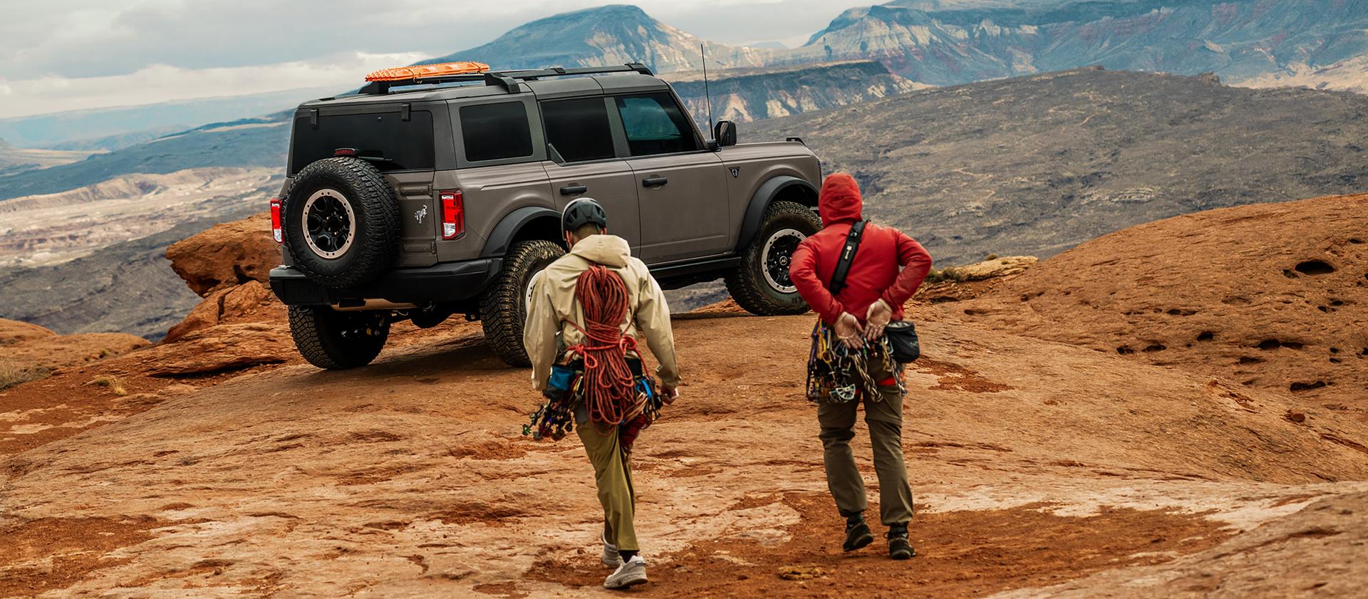 Two hikers approaching a 2026 Ford Bronco® SUV parked near a scenic overlook