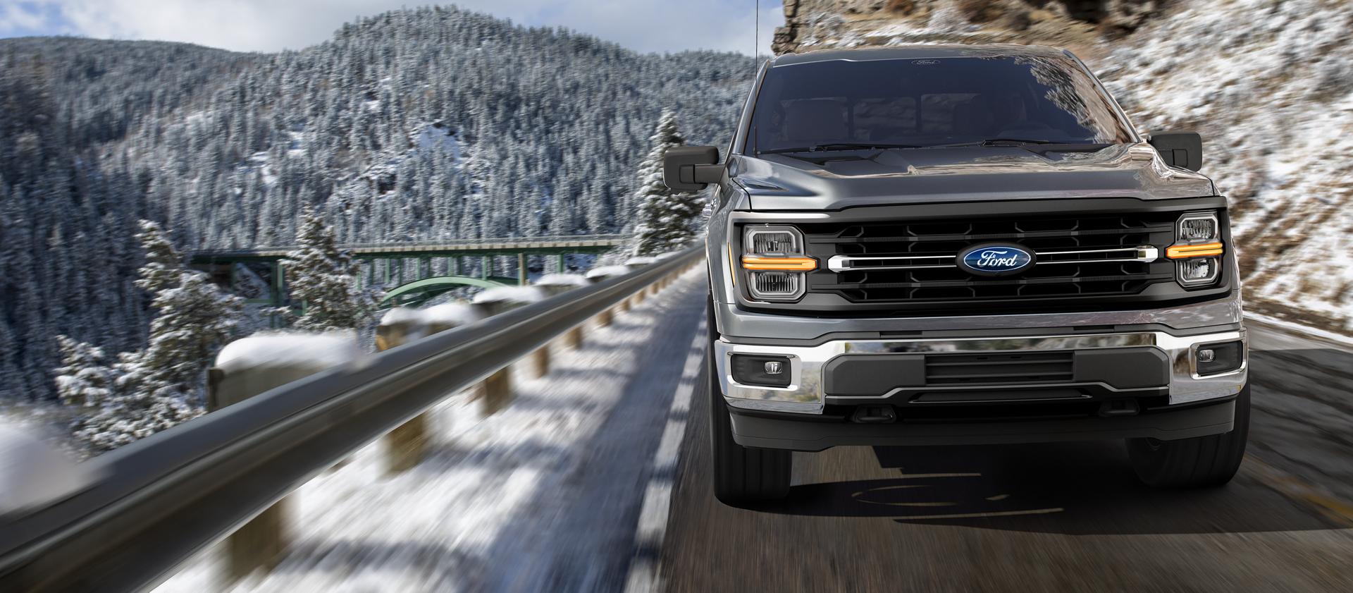 2026 Ford F-150® Lariat® model being driven on a mountain roadway with snow covered mountains