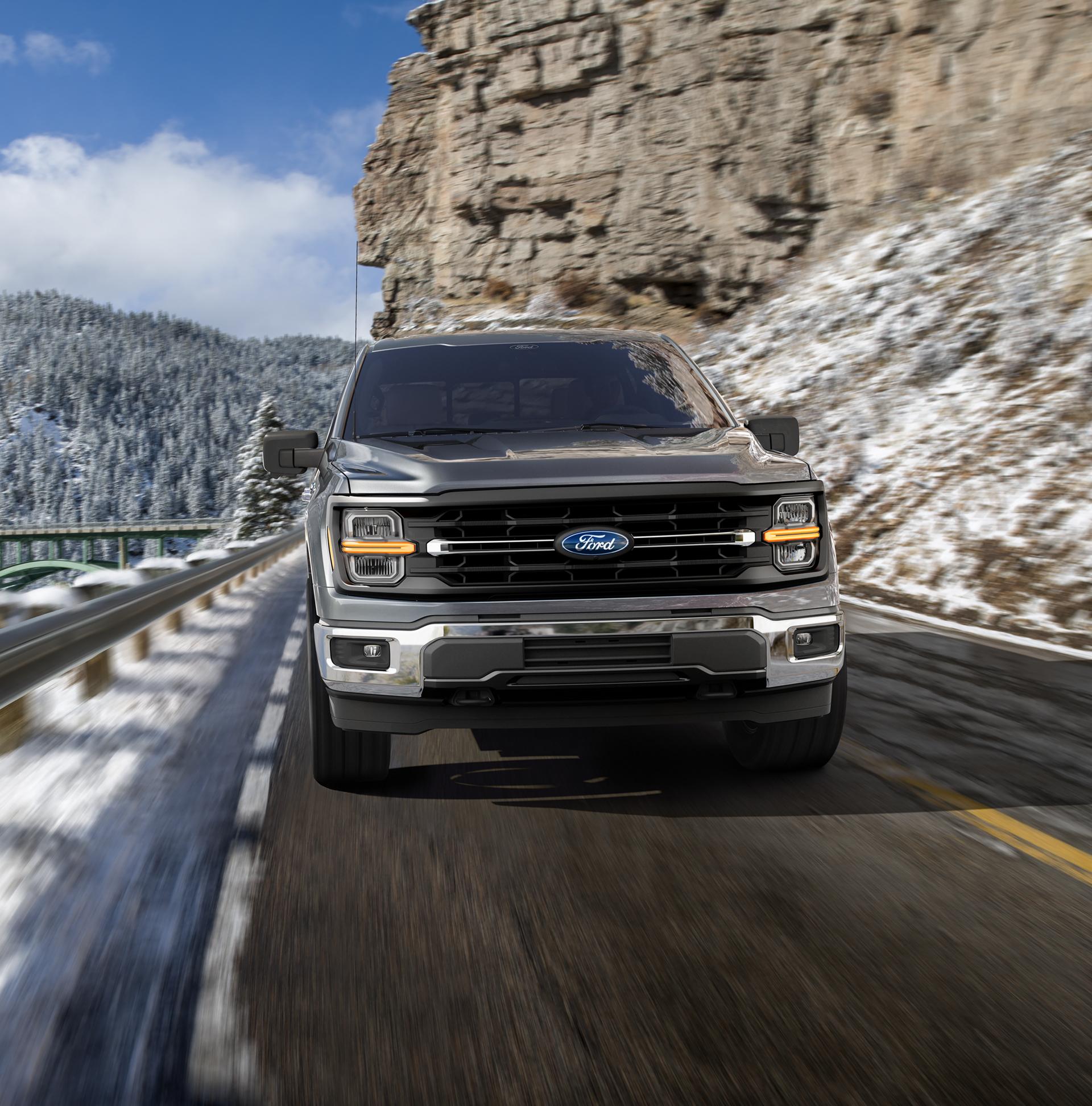 2026 Ford F-150® Lariat® model being driven on a mountain roadway with snow-covered mountains