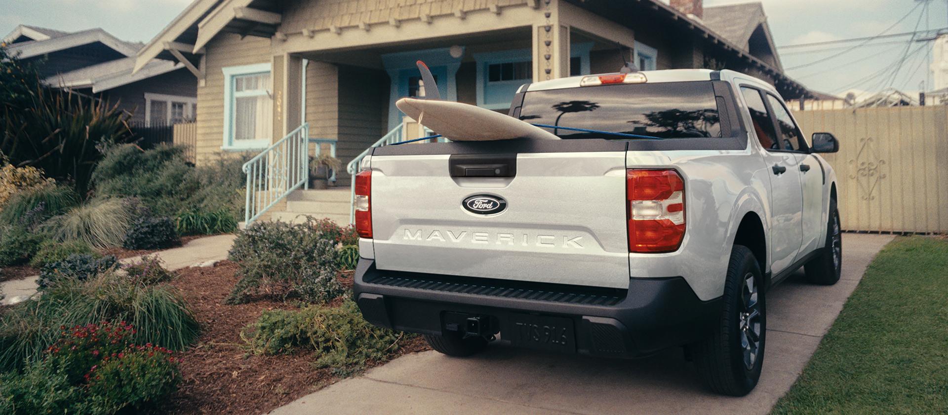 Rear view of a 2026 Ford Maverick® pickup with a paddle board sticking out of the truck bed parked in front of a home