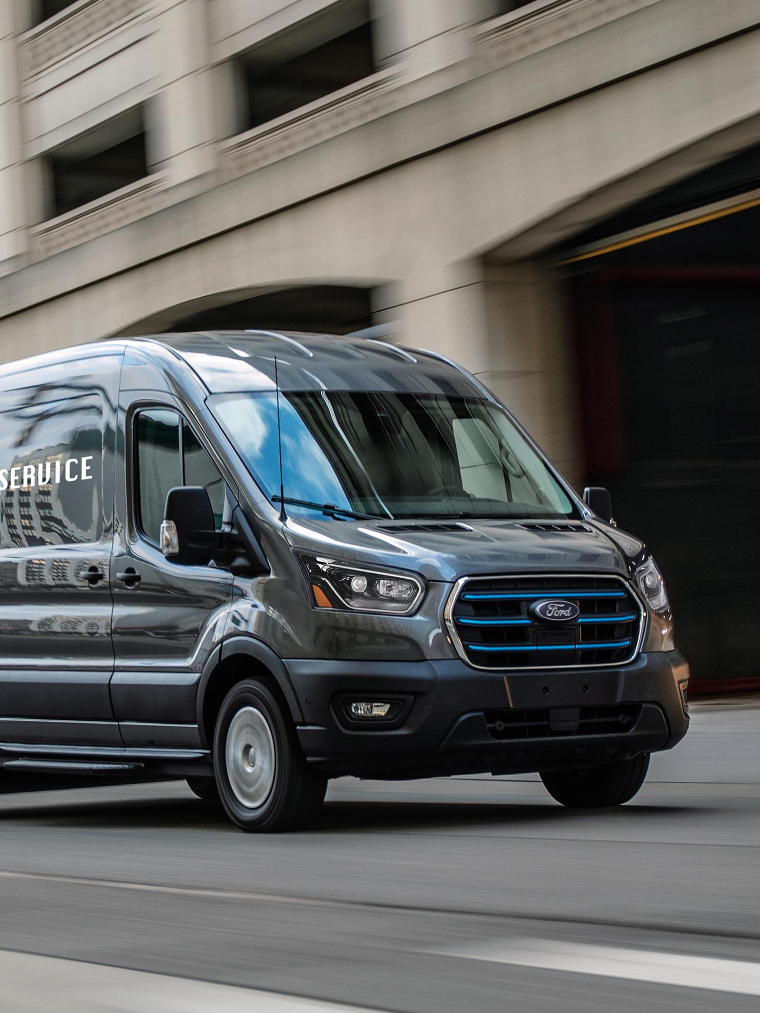 A Grey 2027 Ford Transit® Van driving in a city, blurring with motion