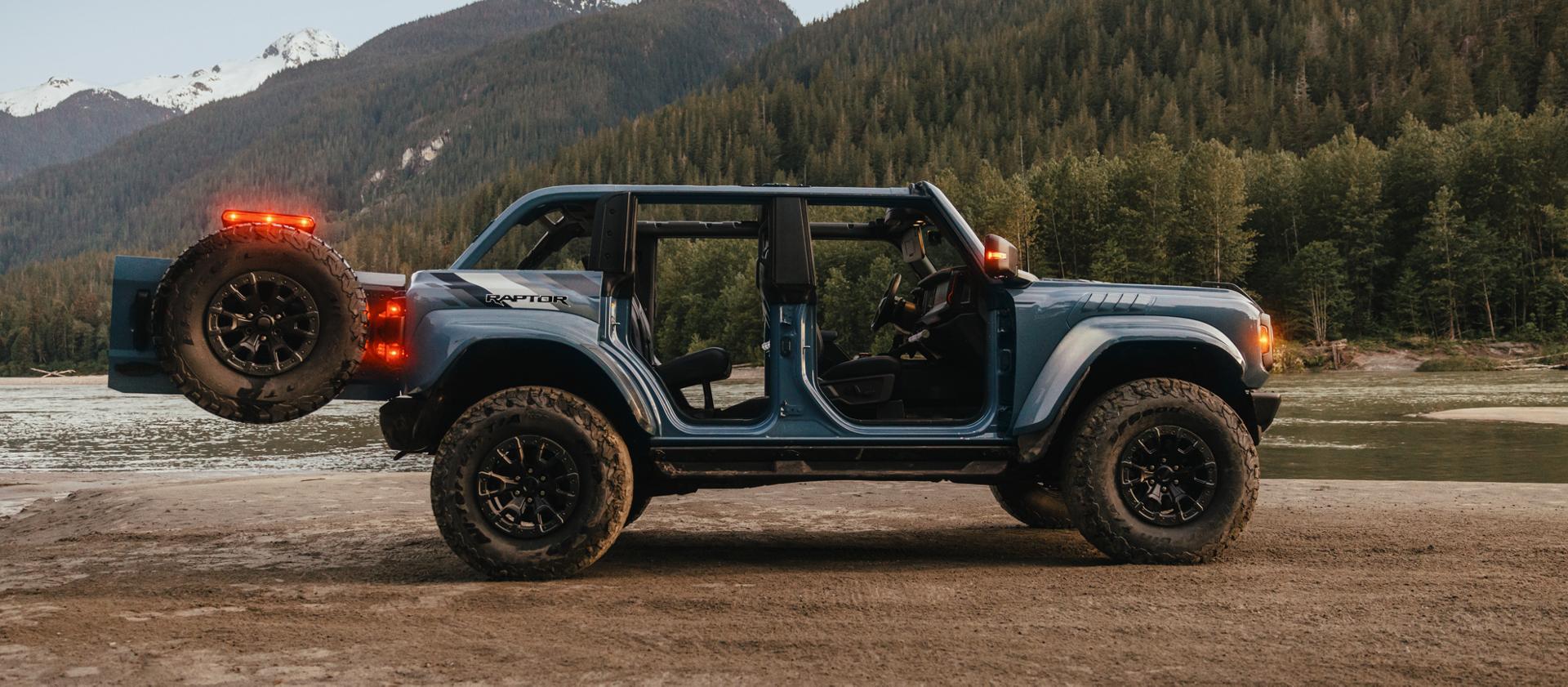 A 2025 Ford Bronco® SUV with the doors removed and the tailgate open, parked on a mud flat near a mountain lake