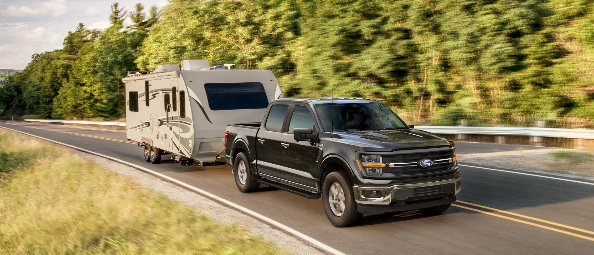 2025 Ford F-150® XLT model in Darkened Bronze Metallic pulling a camper on a tree-lined road