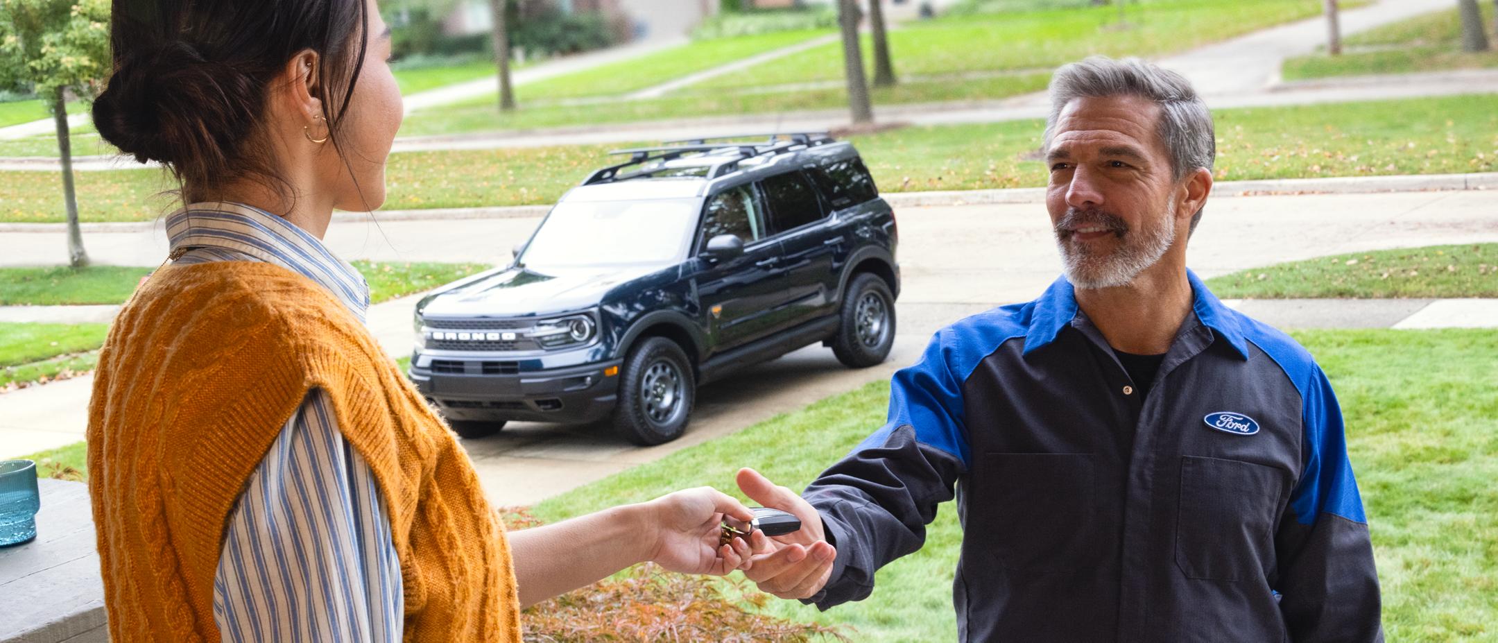 A Ford owner hands their Bronco Sport keys to a Ford Service technician at their home for Pickup and Delivery service.
