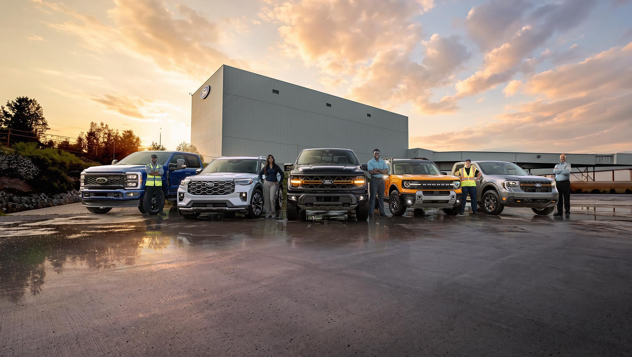 Ford employees standing beside Ford vehicles parked in front of the Ford Oakville Assembly Complex.