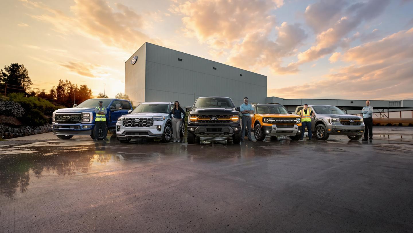 Ford employees standing beside Ford vehicles parked in front of the Ford Oakville Assembly Complex.