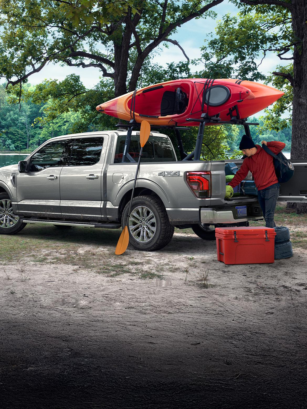 Grey F-150 with a canoe mounted on bed racks parked by a lake.