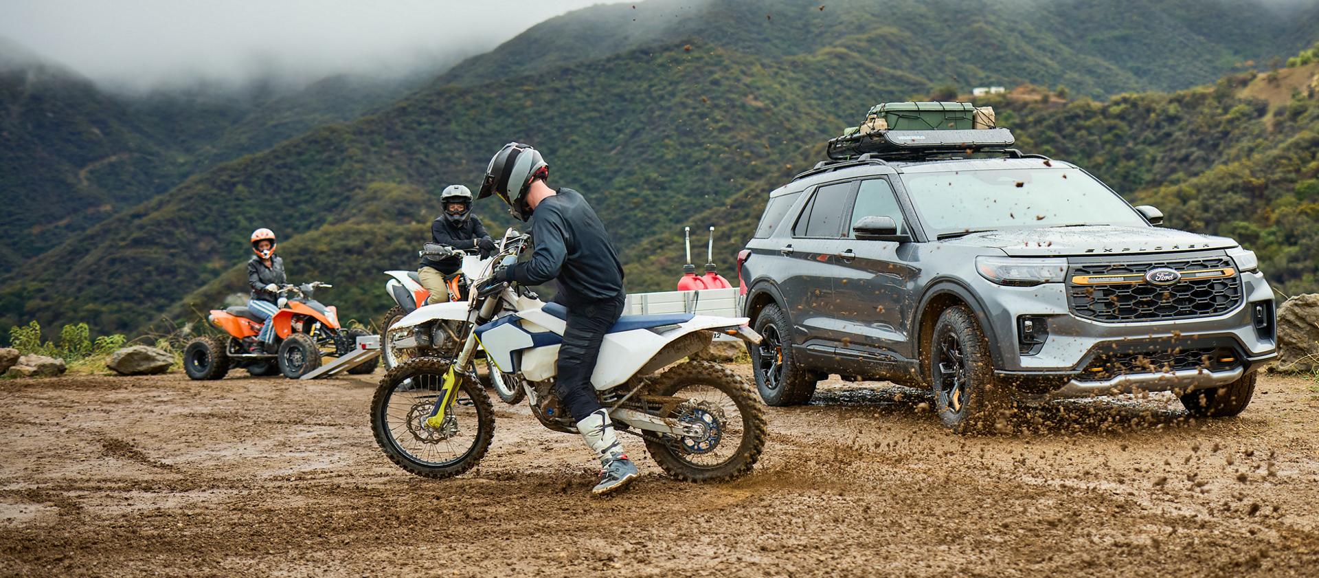 Three people riding dirtbikes through the mud near a 2026 Ford Explorer® SUV