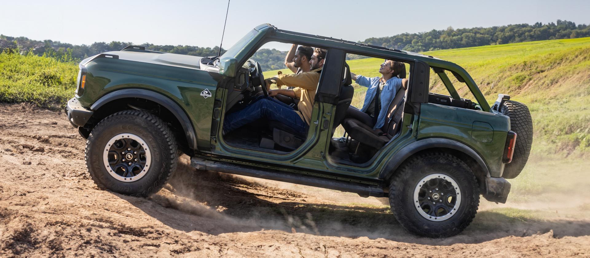 Several people riding on a hilly dirt trail in a 2025 Ford Bronco® SUV with the doors and roof removed