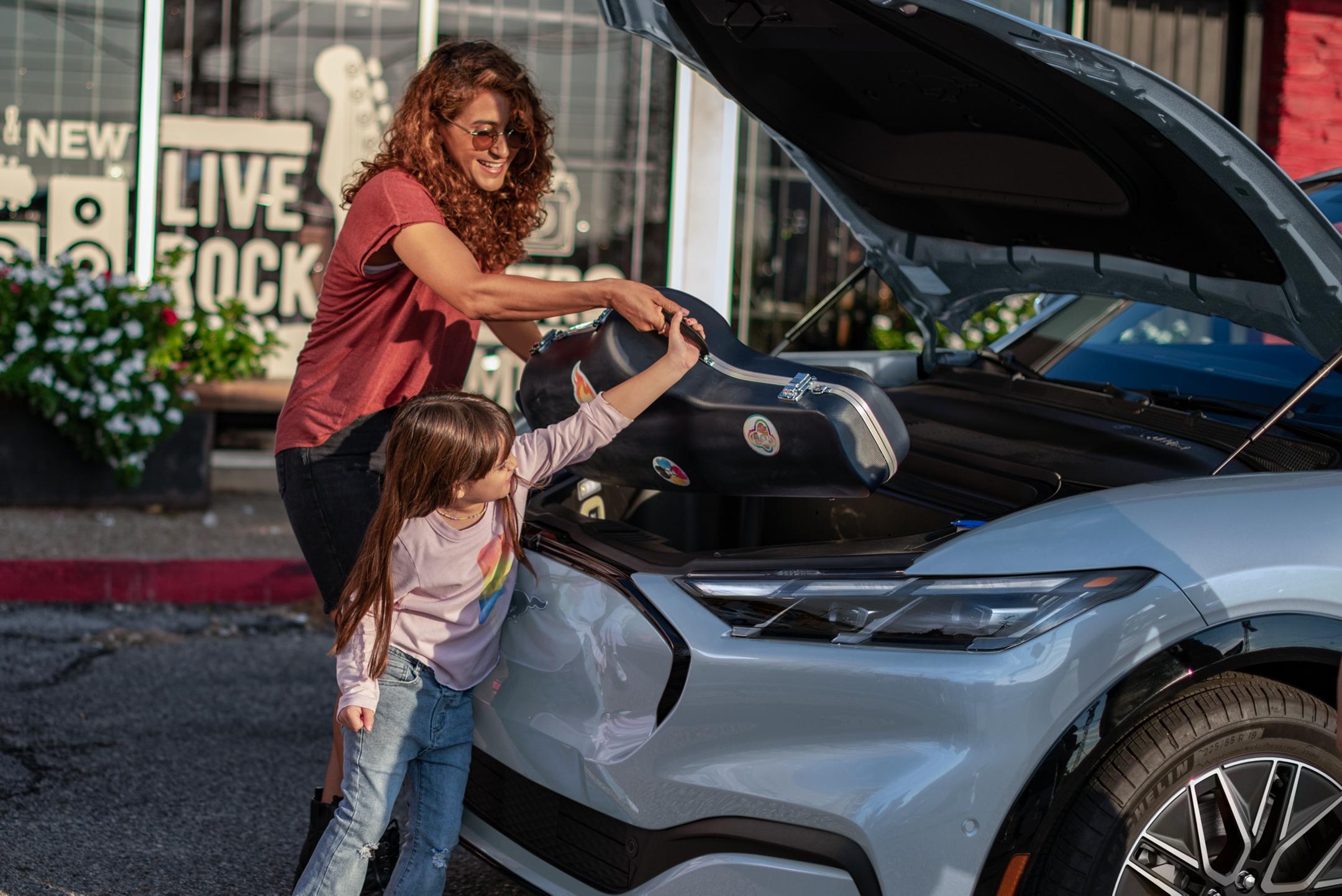 Parent and child load items into the frunk of a Mustang Mach-E.