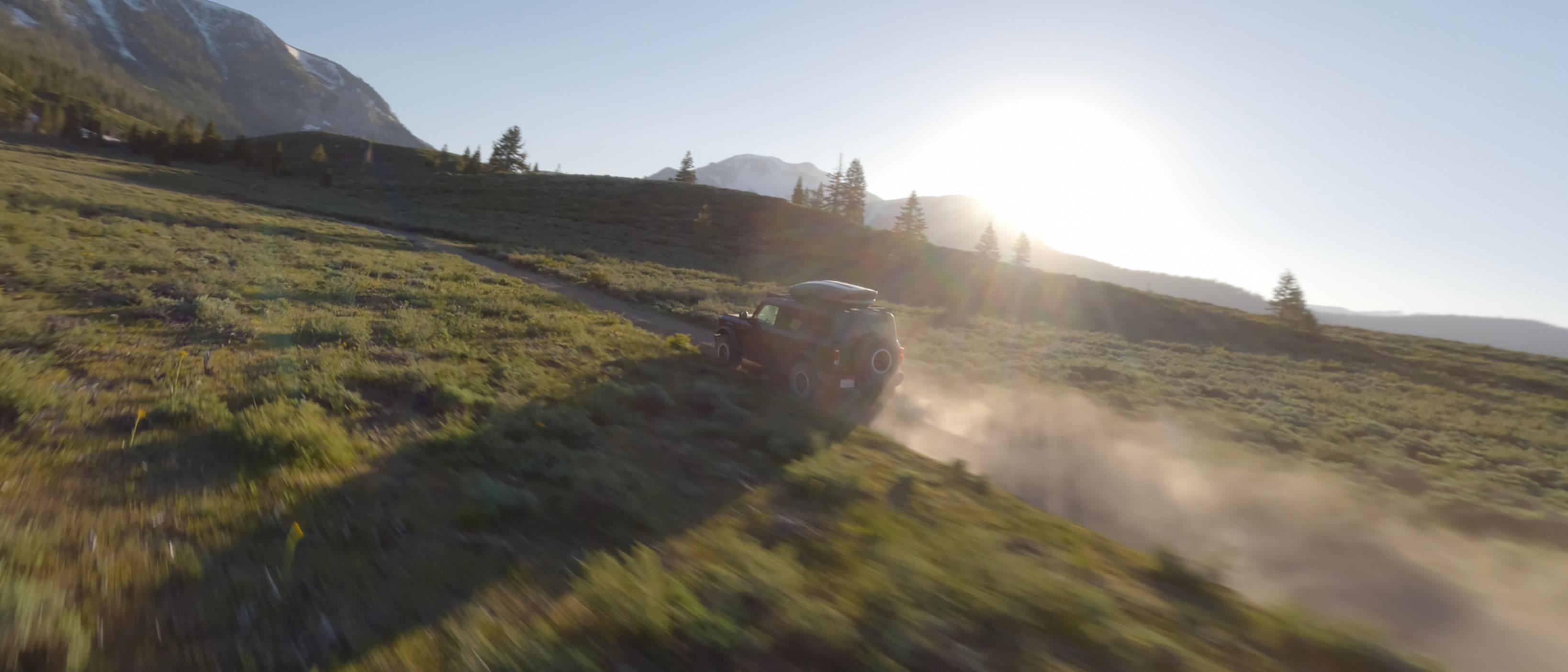 A 2026 Ford Bronco® SUV kicking up dust as it's driven through a grassy valley