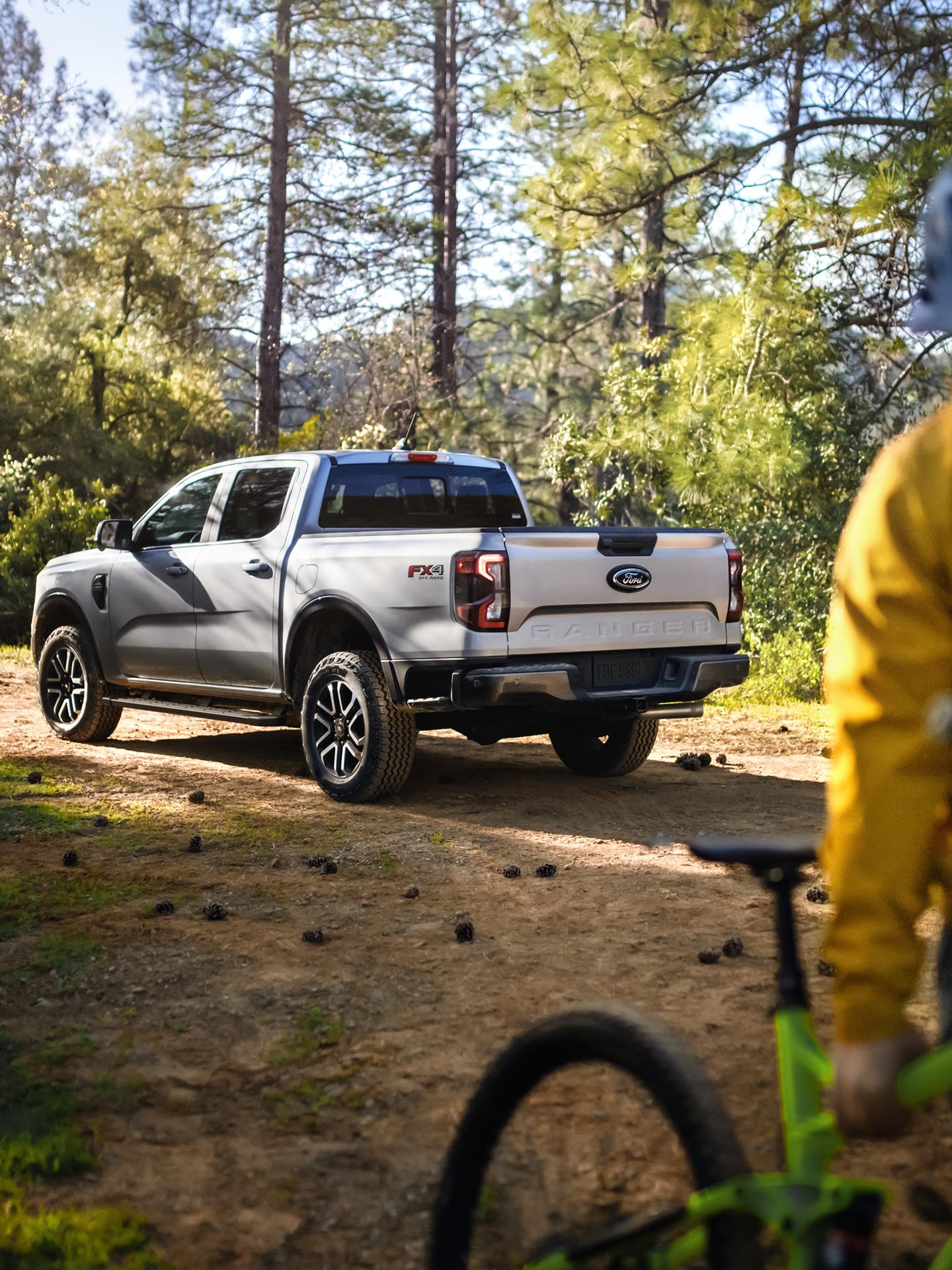 2026 Ford Ranger® Lariat® model parked in the woods. The truck's owner is pulling away on a bike