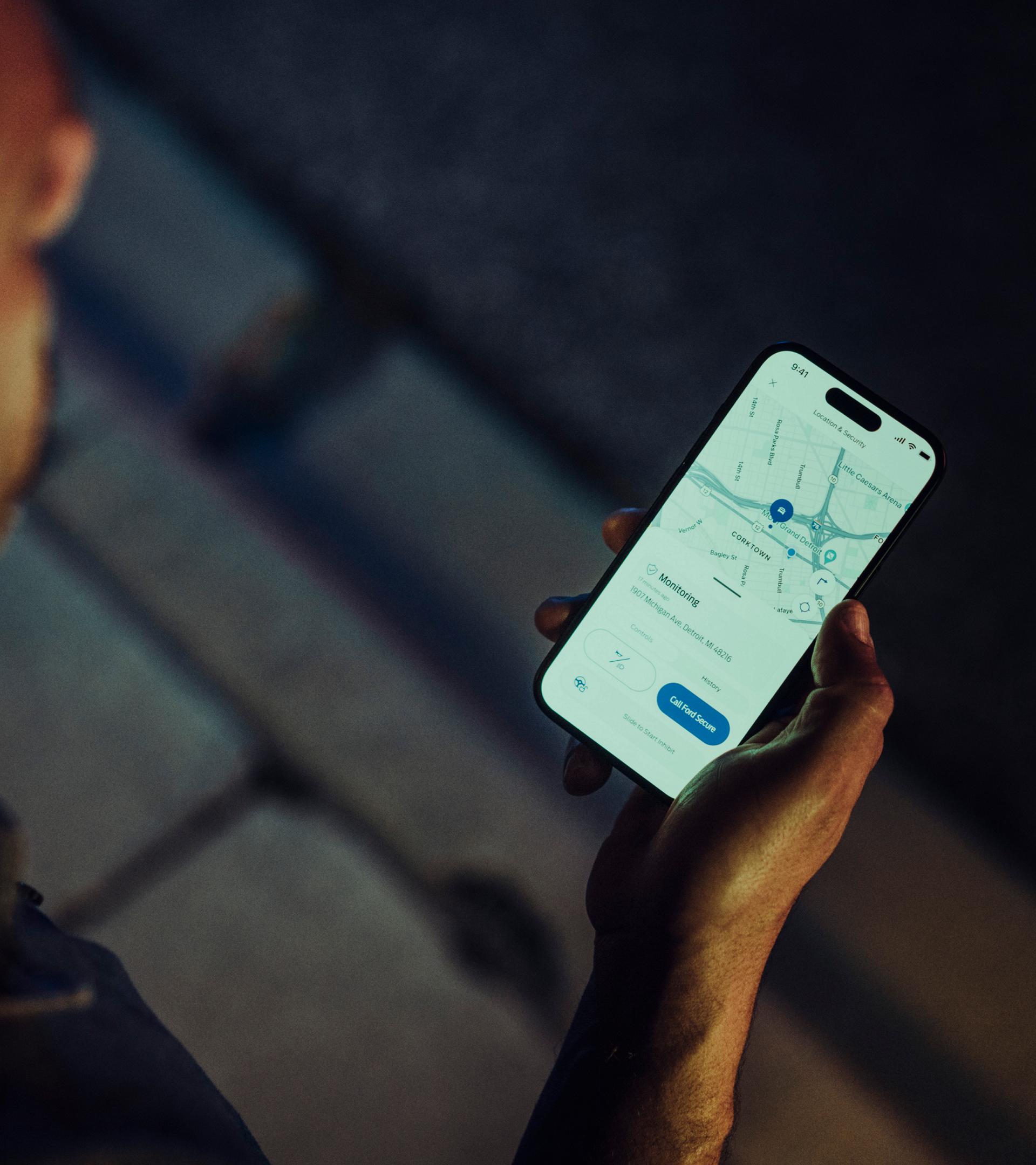 Person holding a smartphone displaying the vehicle locator screen in the Ford app.