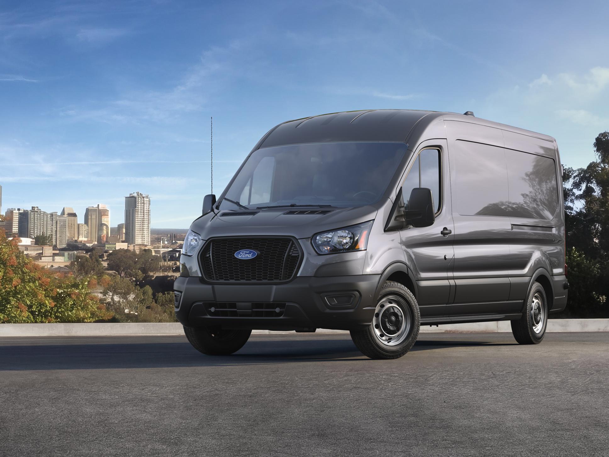 A grey 2027 Ford Transit® Van parked on an overlook with a modern city skyline in the background