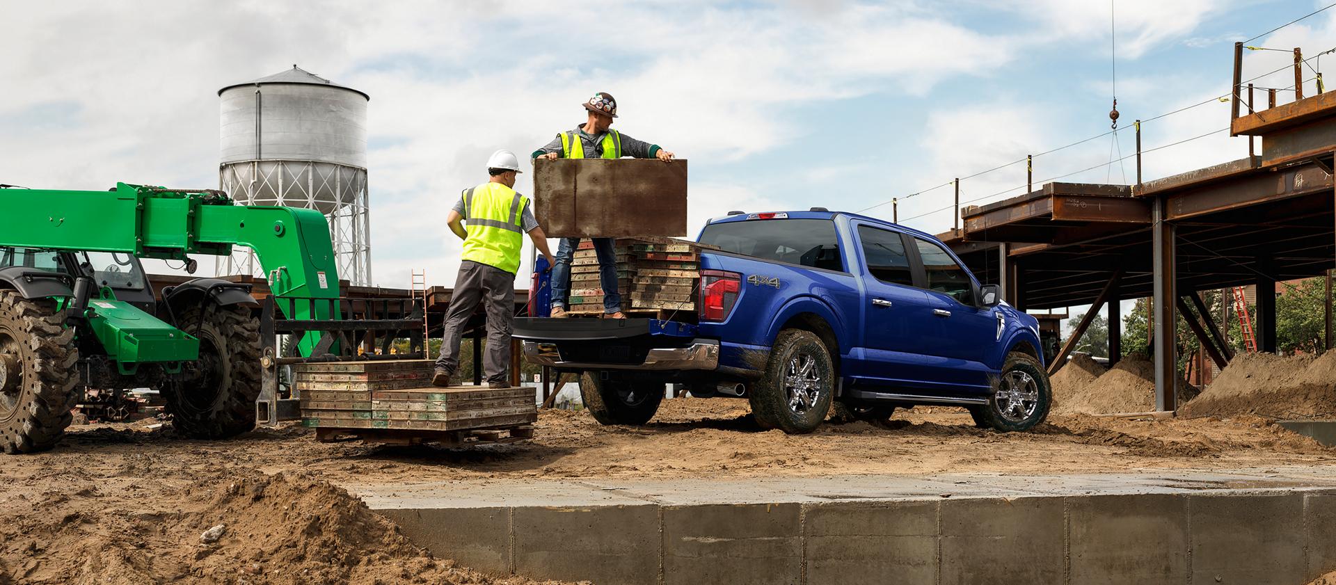 Two men unloading construction materials from the bed of a 2026 Ford F-150® STX® FX4 pickup in Antimatter Blue Metallic