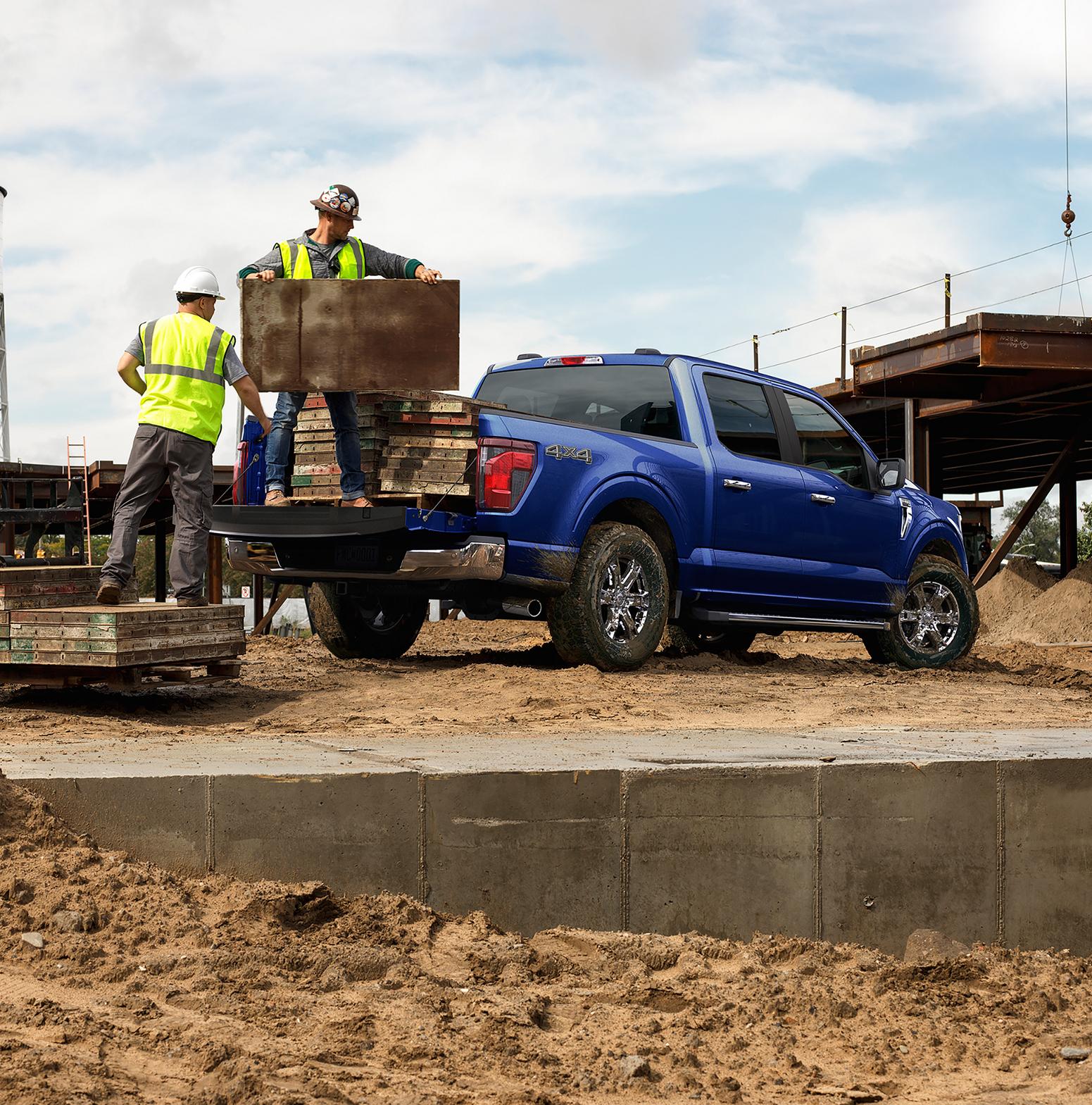 Two men unloading construction materials from the bed of a 2026 Ford F-150® STX® FX4 pickup in Antimatter Blue Metallic