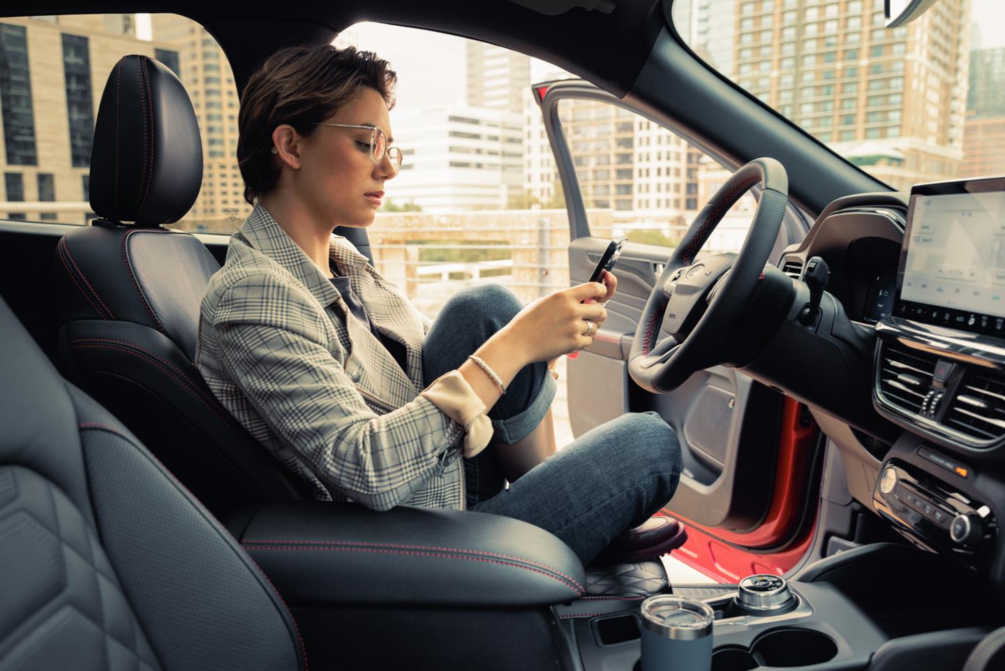 Person holding smartphone sitting in a parked vehicle with the driver side door open