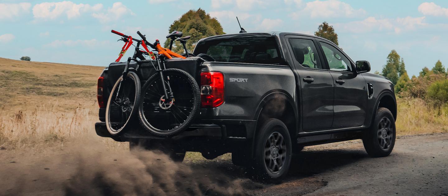 A 2026 Ford Ranger® truck being driven on a dirt road with three bicycles in the bed
