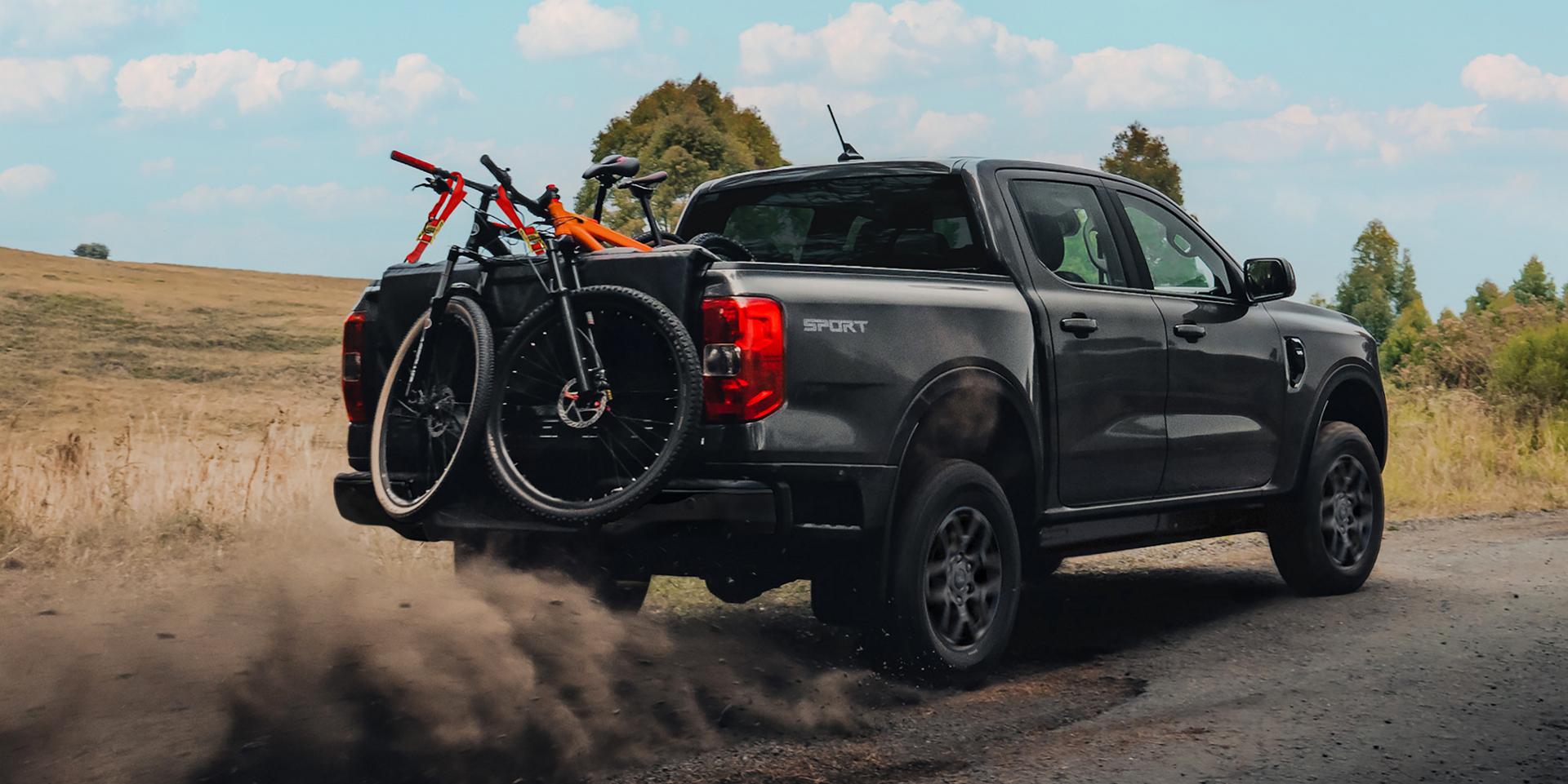A 2026 Ford Ranger® truck being driven on a dirt road with multiple bikes in the bed