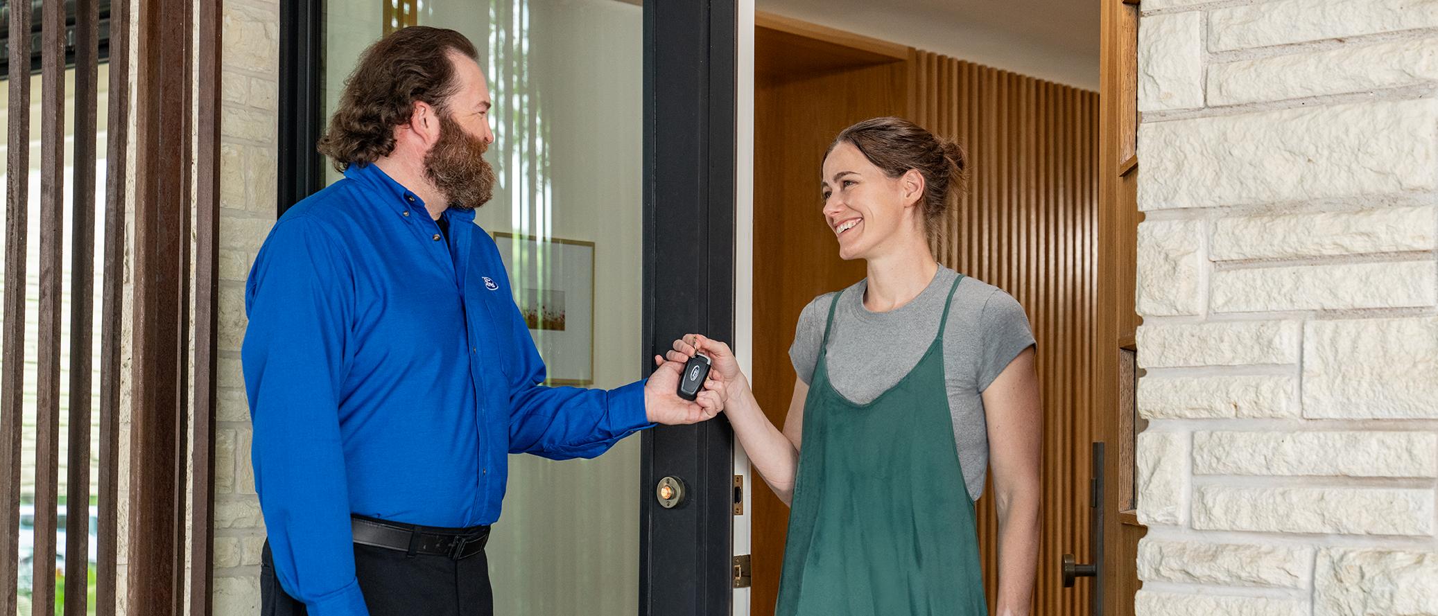 A Ford Pickup & Delivery driver hands the keys back to a Ford owner standing in the doorway of a home.