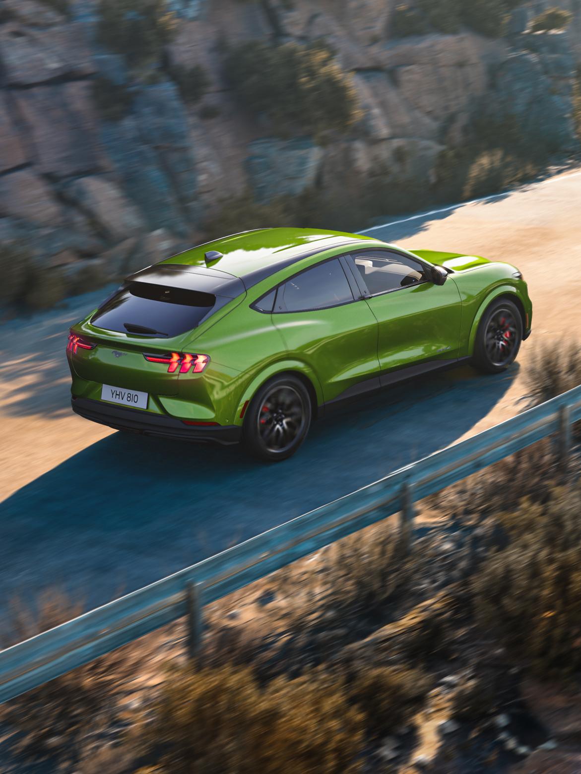 A green Mustang Mach-E driving on a mountain road.