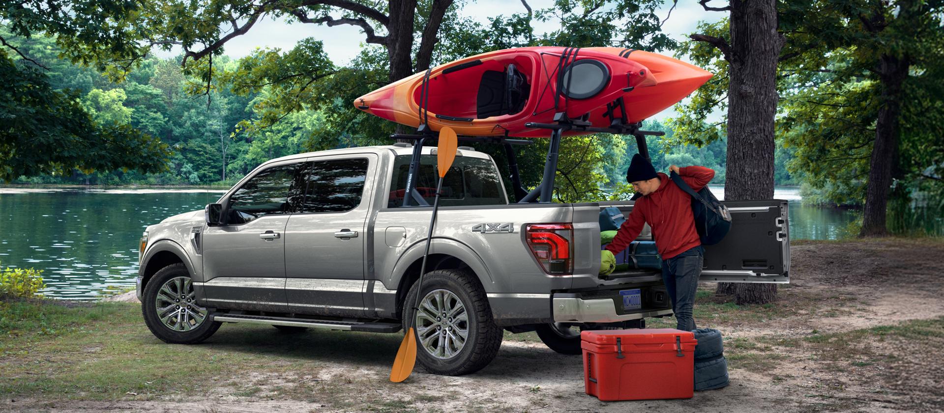 F-150 parked near a lake with mounted canoe and a person unloading gear from the bed.