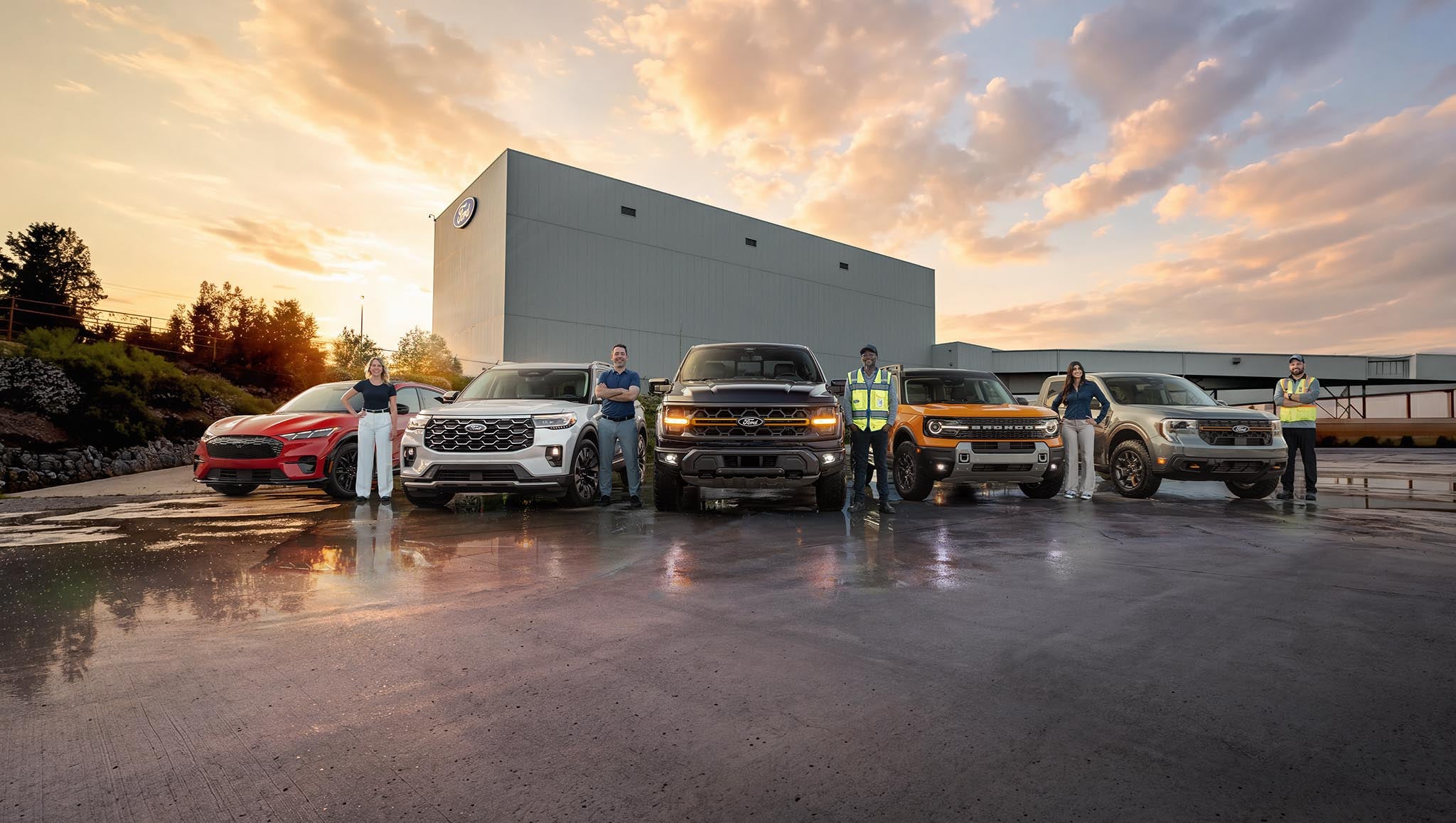 Ford employees standing beside Ford vehicles parked in front of the Ford Oakville Assembly Complex.