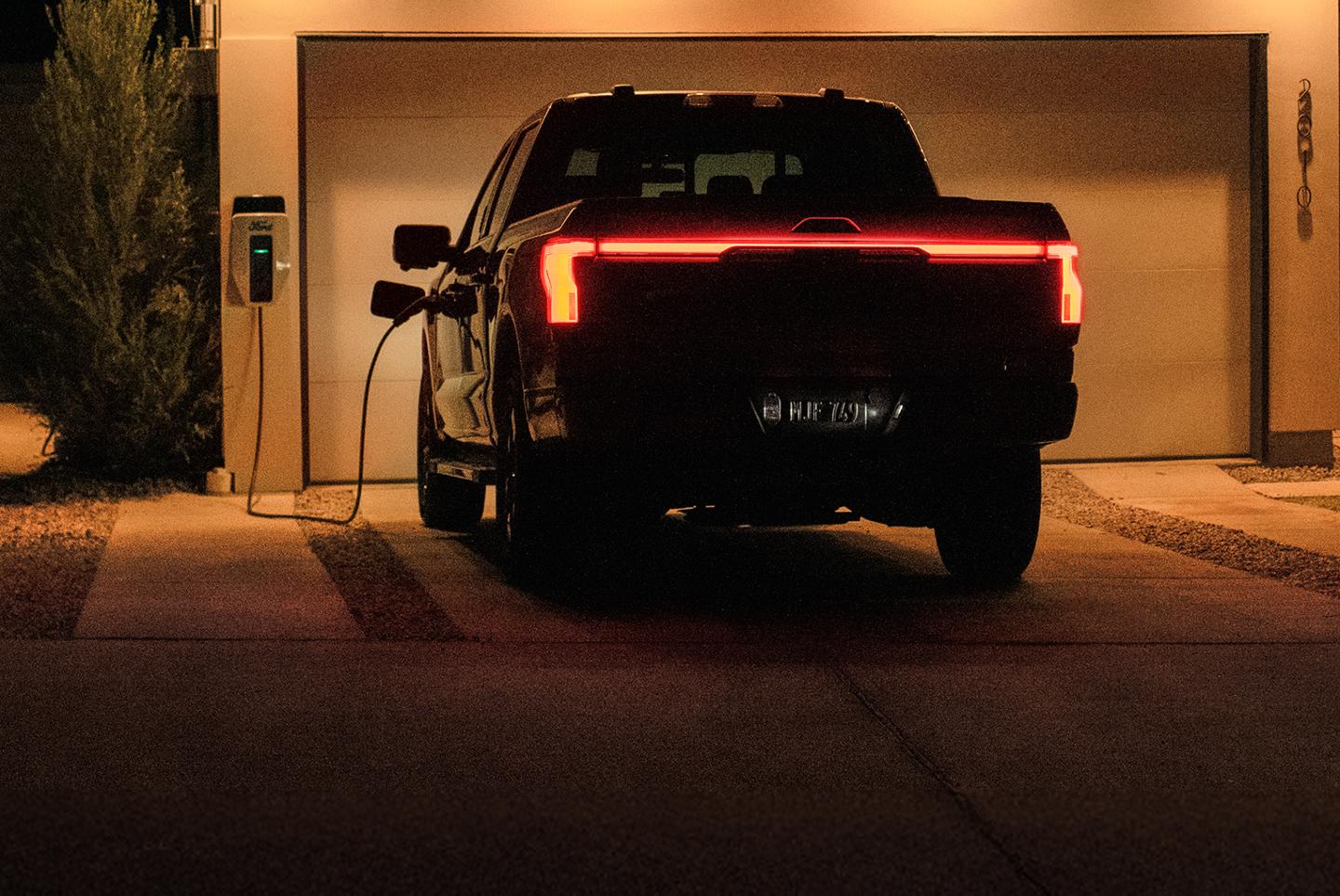 F-150 Lightning parked in a residential driveway at night and plugged into a home charging station.