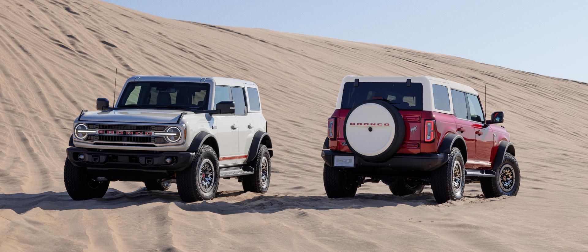 Two 2026 Ford Bronco® SUVs with the available 60th Anniversary Package parked on a sand dune on a sunny morning