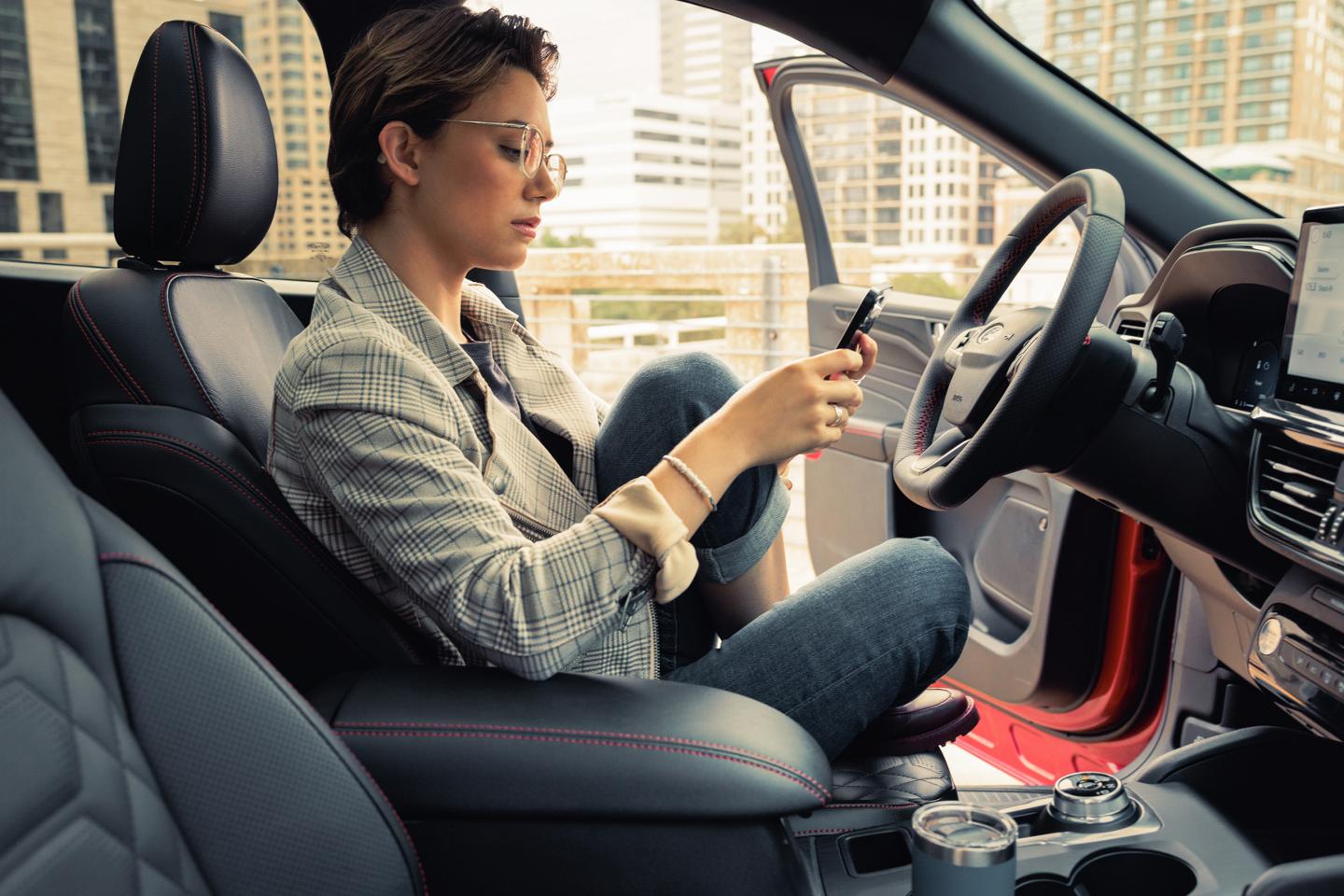 Person holding smartphone sitting in a parked vehicle with the driver side door open