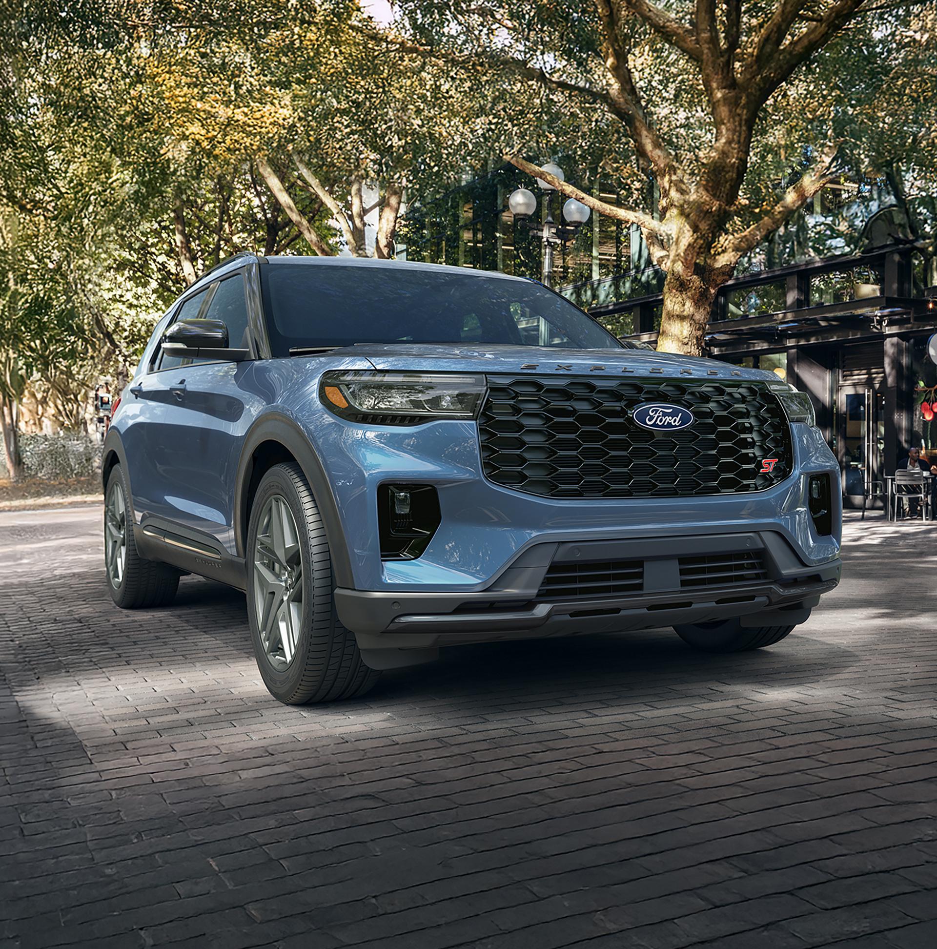 A 2027 Ford Explorer® SUV being driven down a tree-lined commercial street