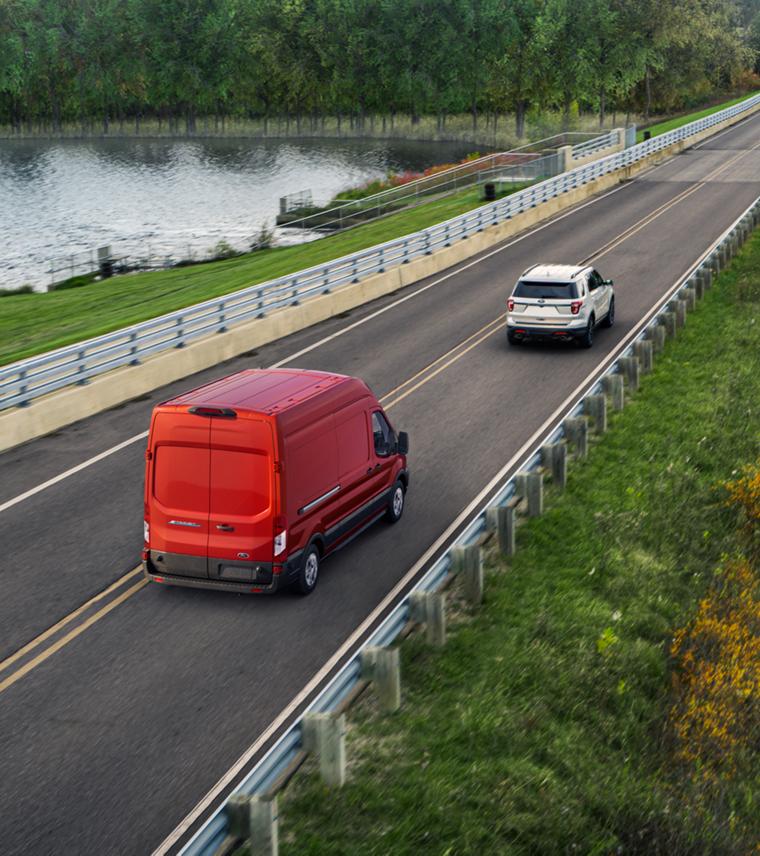 A red 2025 Ford E-Transit™ driving down a country highway