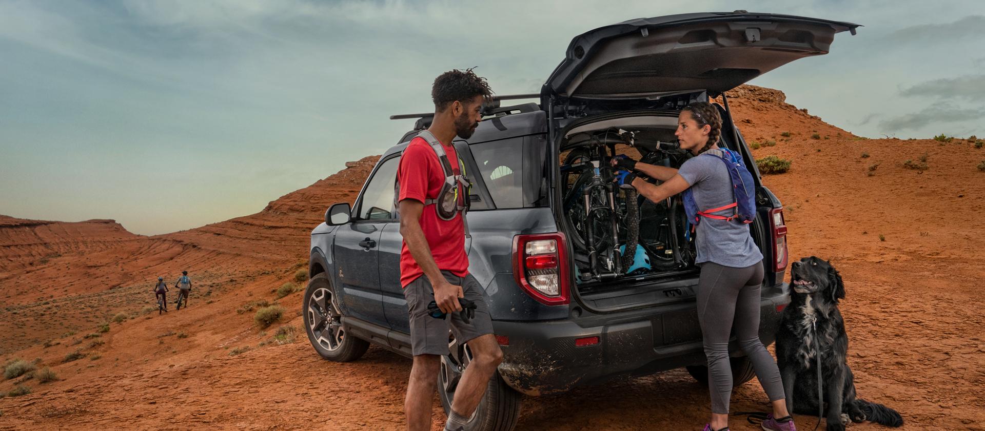 2026 Ford Bronco Sport® SUV parked in the desert with two people standing outside of the vehicle, wearing hiking gear with their dog