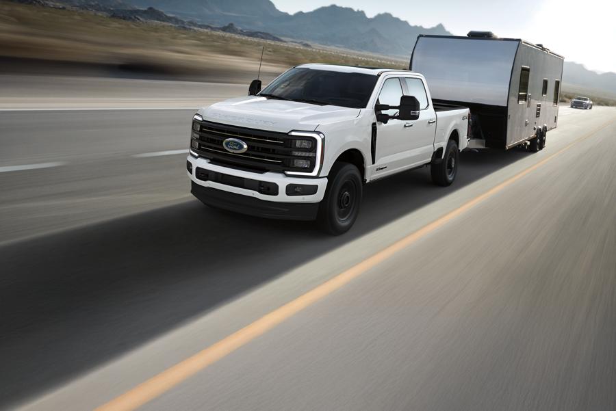 A white ford pulls a camping trailer down a highway.