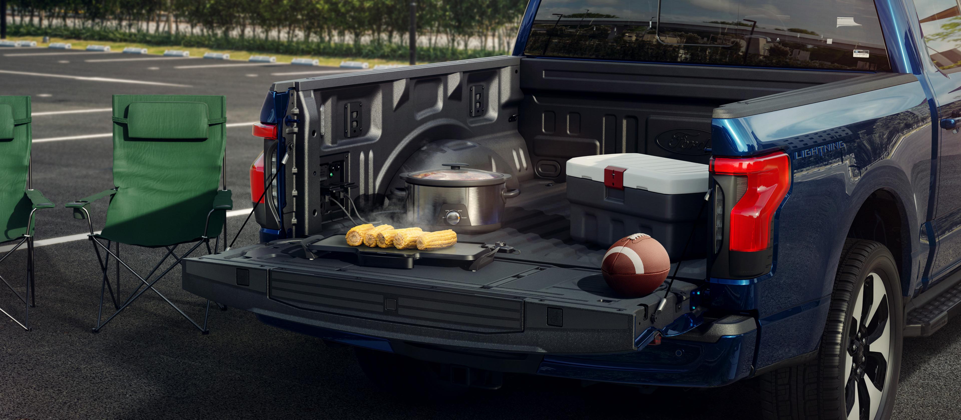 Rear of a 2025 Ford F-150® Lightning® pickup with the tailgate open, with items plugged into the Pro Power Onboard™ outlets