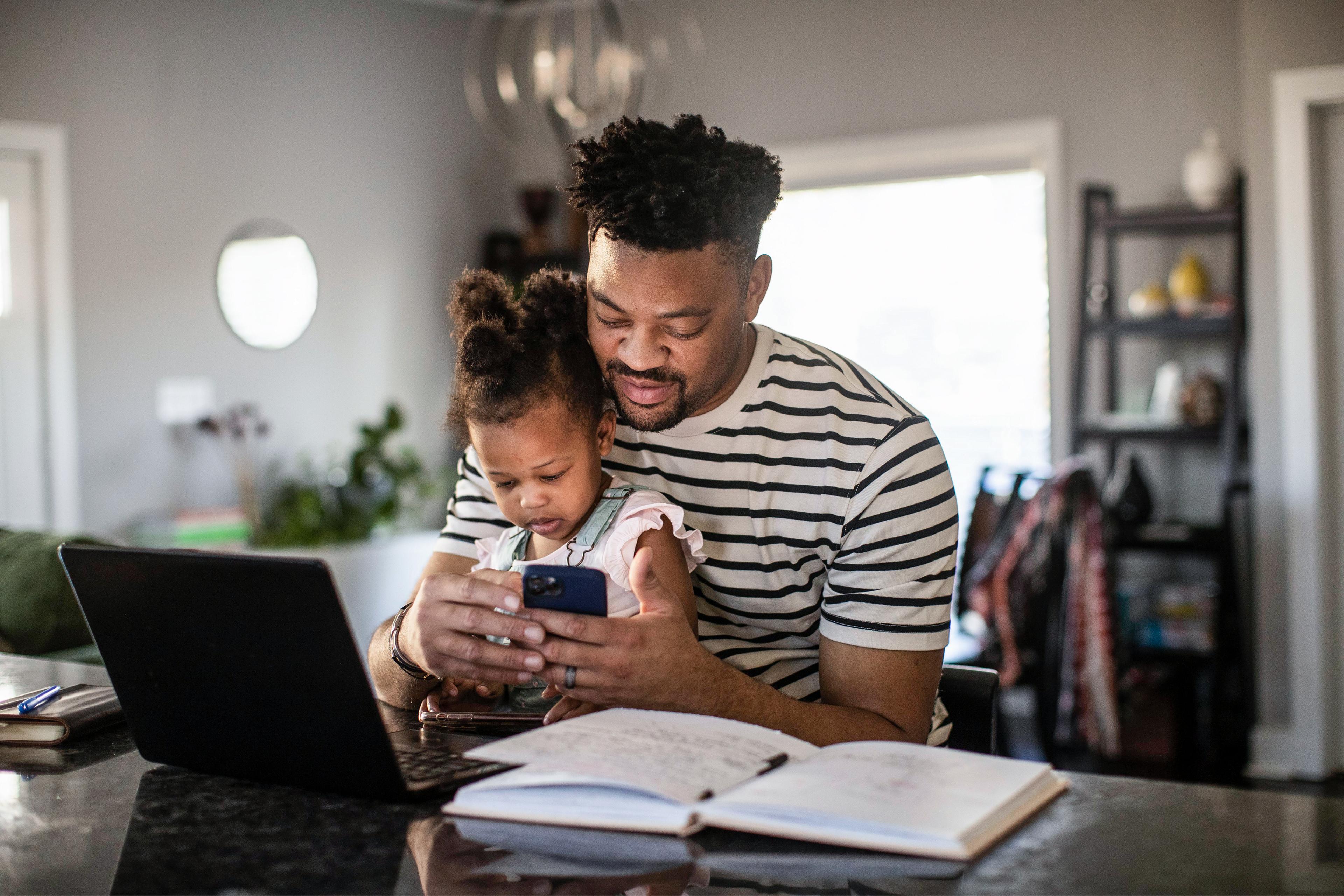 A man holds his child in his lap while interacting with the Ford app on his phone