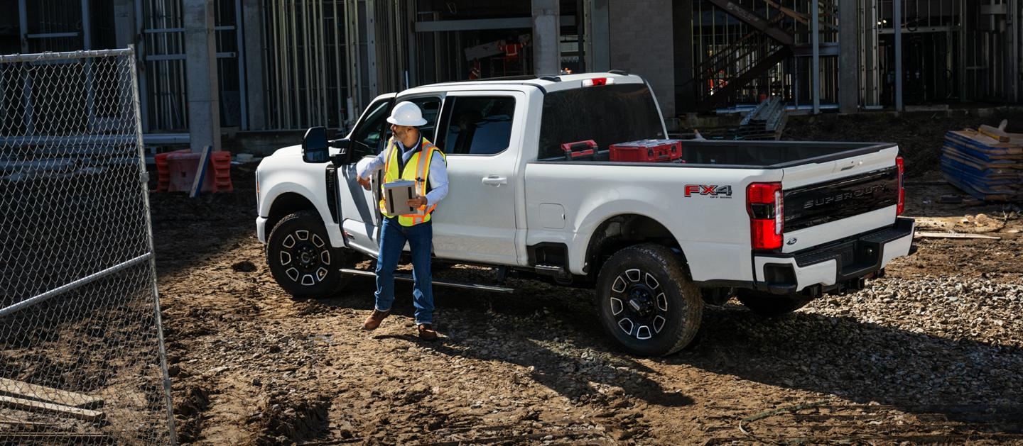 Construction worker stands next to a white Ford Super Duty truck at a construction site. 