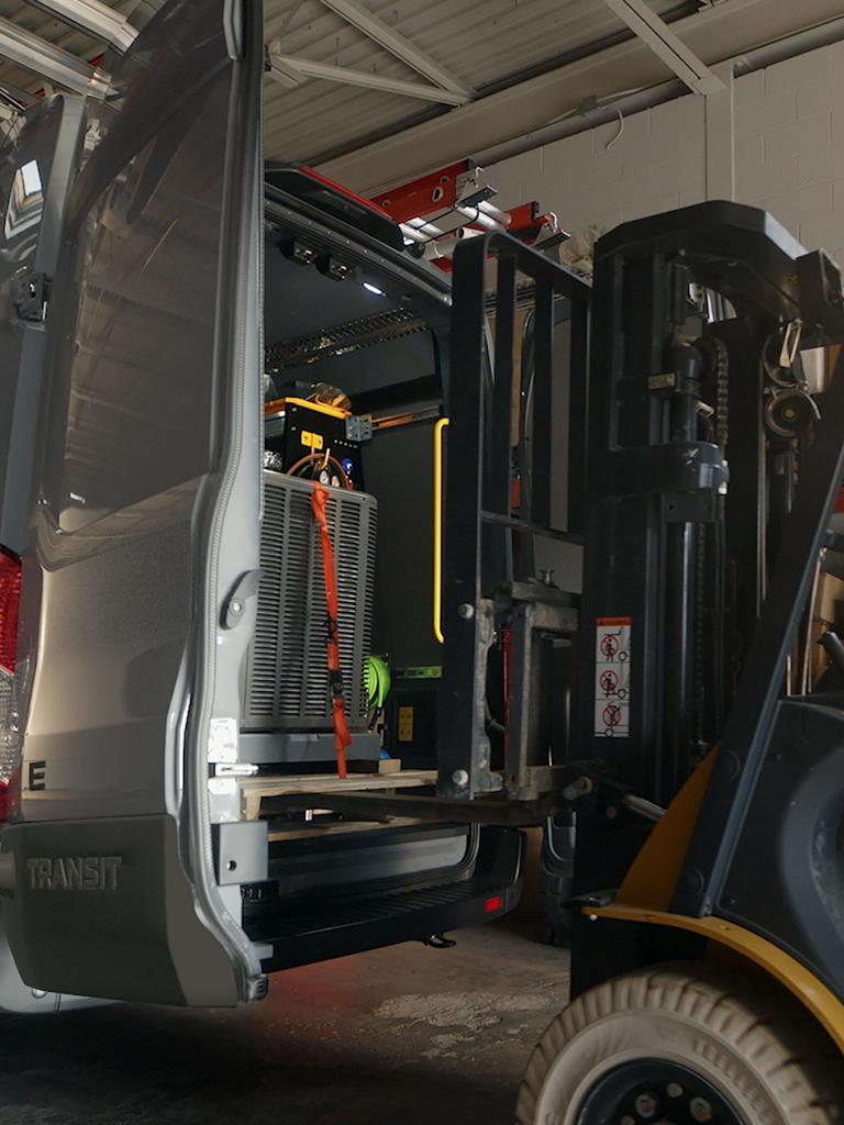 A forklift loads sacks into the back of an open red 2027 Ford E-Transit™ Cargo Van, parked outside a building