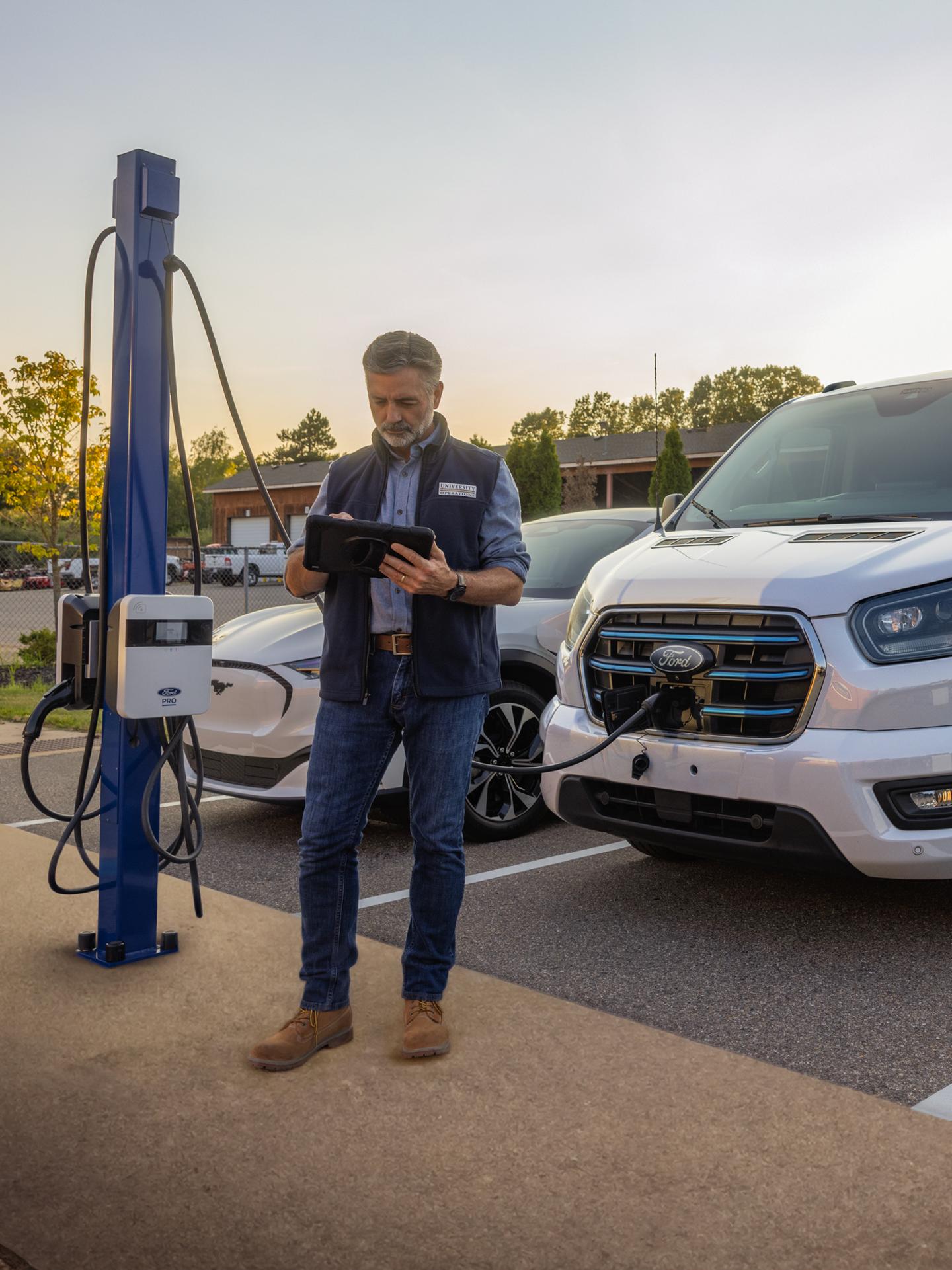 A person standing in front of a parked and charging Ford E-Transit.