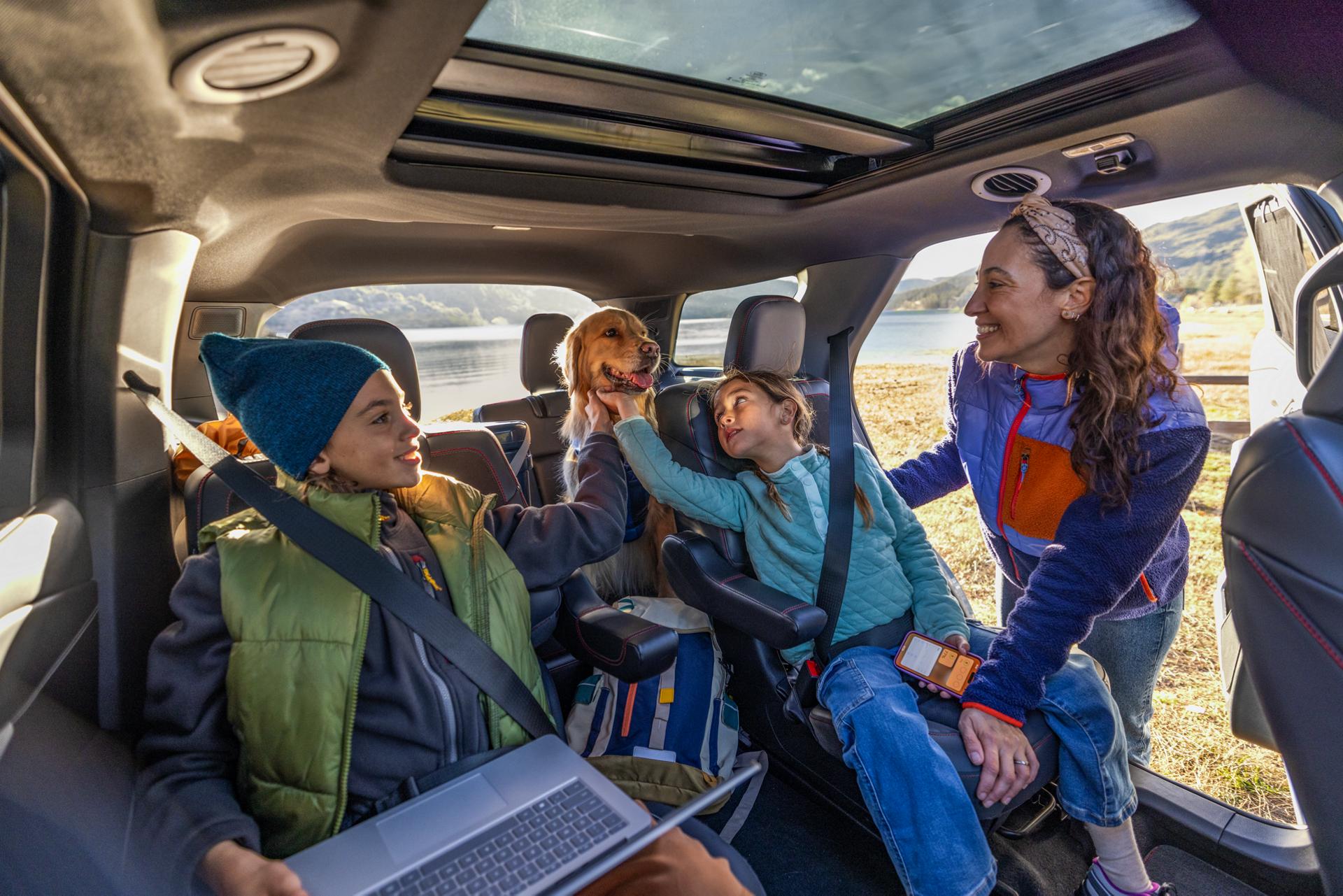 Two kids and a dog in a Ford vehicle with an adult leaning in.