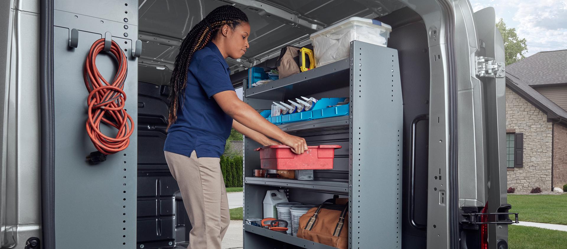 Rear view of a trades person working inside the rear doors of a 2027 Ford Transit® van