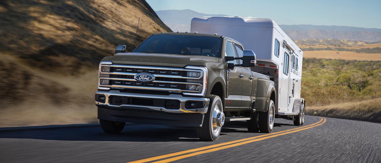 A grey Ford Super Duty truck towing a trailer on a winding mountain road.