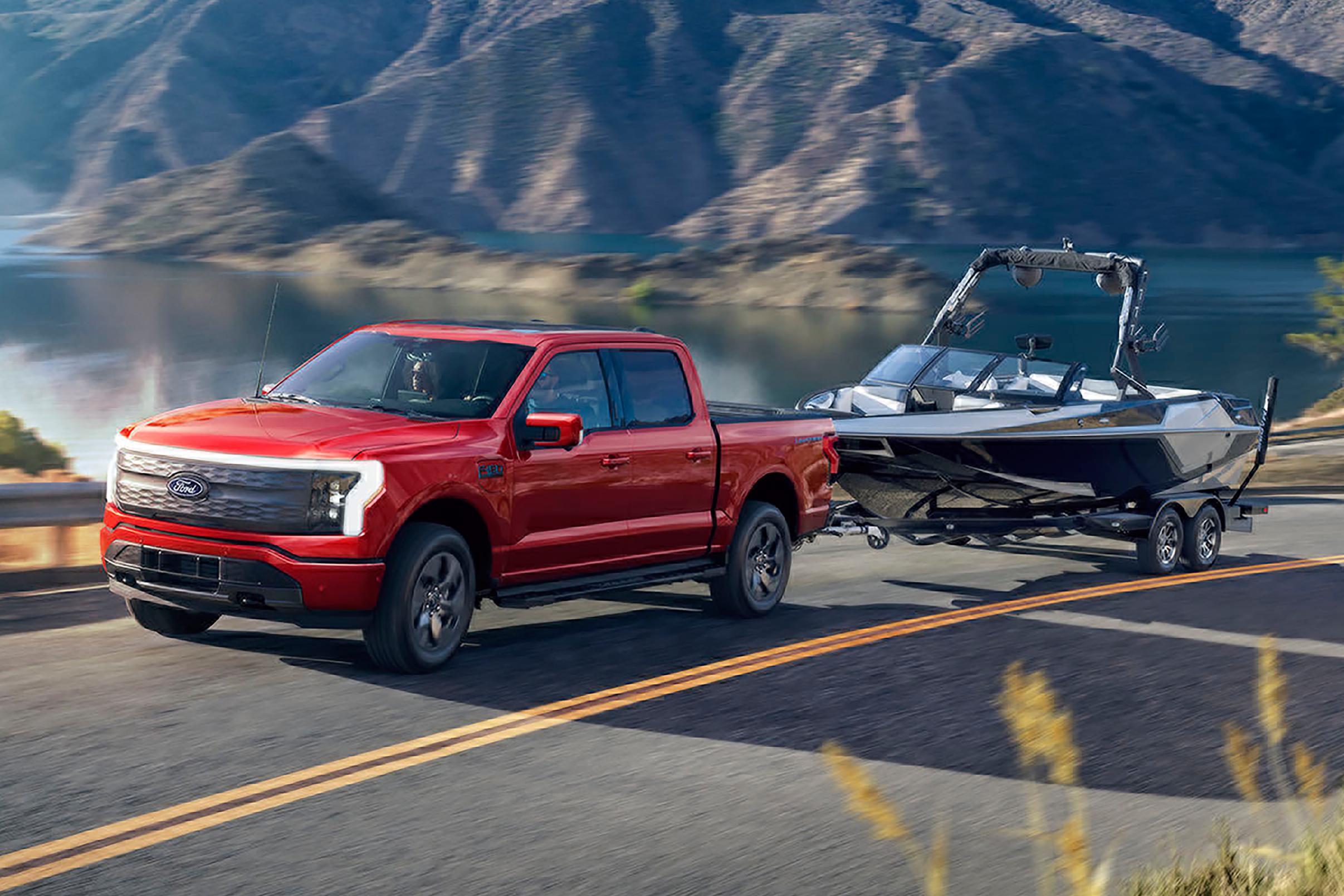 A 2025 Ford F-150® Lightning® hauling a boat on a trailer on a highway near a mountain lake
